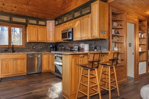 A wooden cabin-style kitchen with built-in appliances, a bar area with stools, and a brick backsplash. - EASY Breezy Lodge  - Sleeps 10 - 3 King Suites - Pets Ok - Fiber Wifi (Deep Gap)