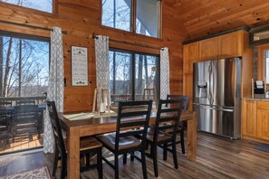 A cabin interior with a wooden dining table, four chairs, a refrigerator, and a kitchen area. - EASY Breezy Lodge  - Sleeps 10 - 3 King Suites - Pets Ok - Fiber Wifi (Deep Gap)