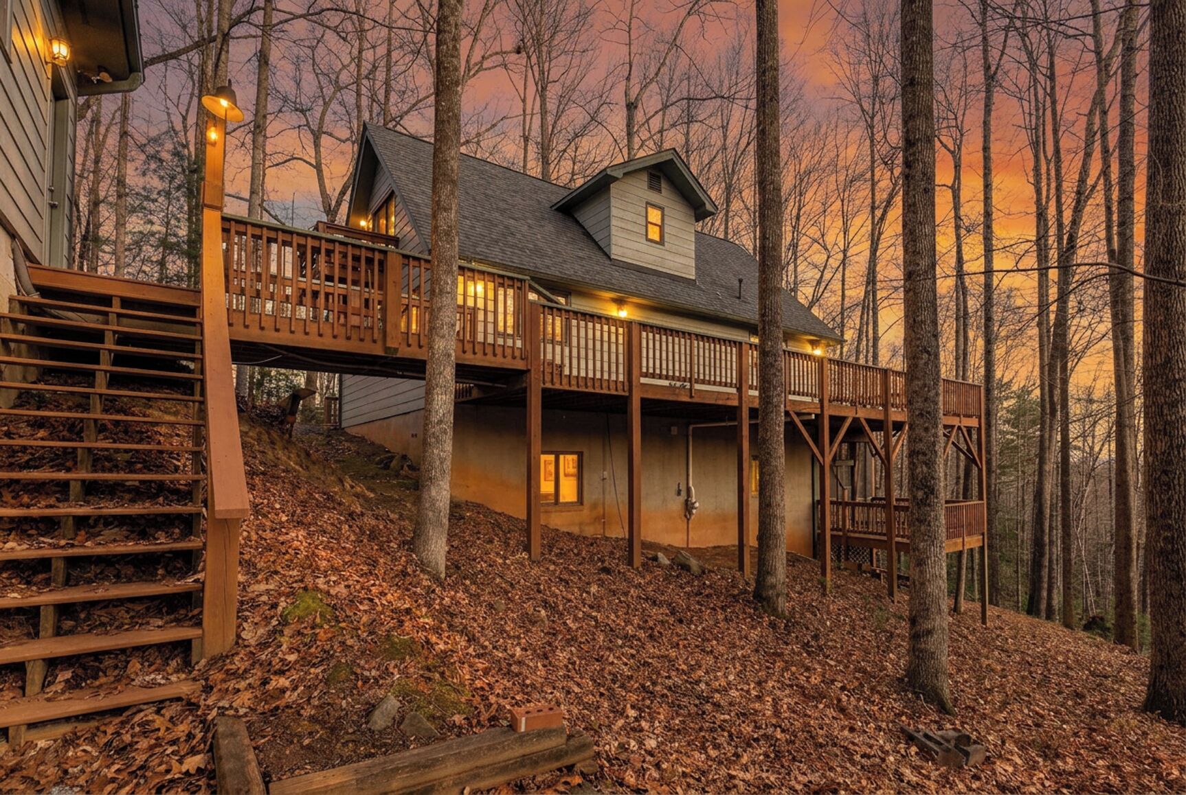 Eine zweistöckige Holzhütte mit einer Holzterrasse und Treppe, umgeben von Bäumen.