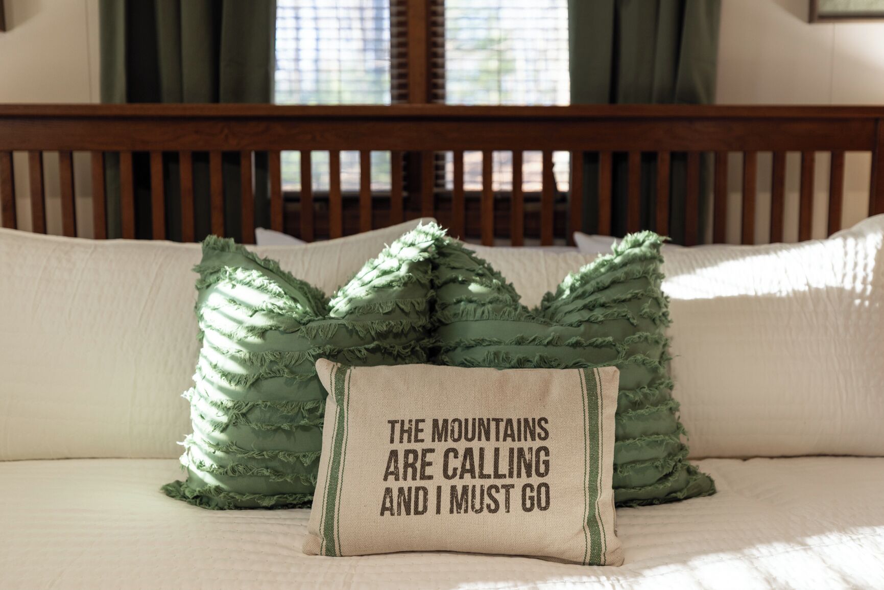 A bed with a wooden headboard, two green pillows, and a beige pillow with text.