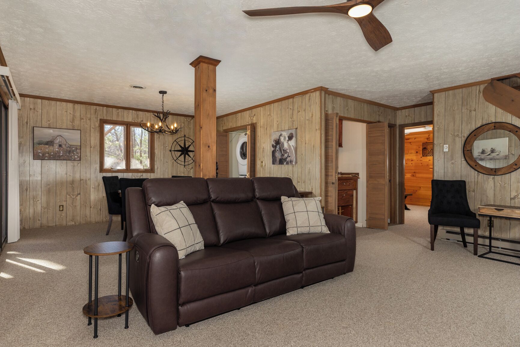 A cozy living room with a brown leather sofa, a round mirror, and a ceiling fan.