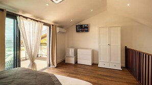 Ein Schlafzimmer mit Bett, Kleiderschrank, Fernseher und einer Schiebetür zum Balkon.