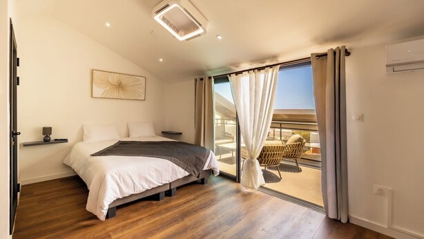 Ein Schlafzimmer mit Bett, Nachttischen, einer Deckenleuchte und Blick auf einen Balkon.
