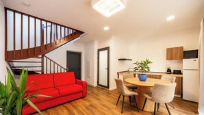 Eine moderne Wohnung mit einer Holztreppe, einem roten Sofa, einem Essbereich mit Tisch und Stühlen sowie einer Küche mit Schränken und Geräten.
