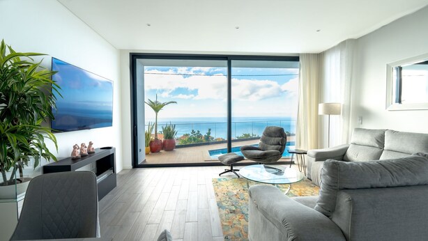 Una sala de estar moderna con un amplio ventanal corredera que da a un balcón con piscina y vista al océano.