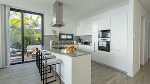 Una cocina moderna con una isla central, electrodomésticos integrados y vistas a un jardín tropical.