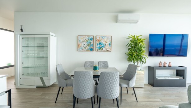 A modern dining area with a glass-top table, grey upholstered chairs, and a potted plant. - Moonlight Villa by LovelyStay (Estreito da Calheta)