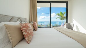 Habitación de hotel con una cama grande, vista al océano y un balcón con una palmera.