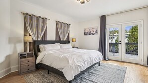 A bedroom with a bed, bedside tables, a nightstand, a lamp, a painting, and a view through a glass door. - Game Room | Family House | Close to Buford Highway (Chamblee)