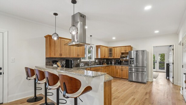 A modern kitchen with wooden cabinets, stainless steel appliances, and a central island with bar stools. - Game Room | Family House | Close to Buford Highway (Chamblee)