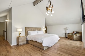 Un dormitorio con una cama de madera, lámparas de noche, un aplique colgante y un sofá.