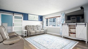 A living room with a beige sofa, a white entertainment unit, a flat-screen TV, and a large window with curtains. - Beautiful, spacious luxury home in Michigan for 12
. (Wyoming)