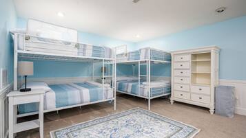 A room with bunk beds, a white dresser, a lamp, and a patterned rug.