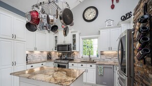 A kitchen with white cabinets, a granite island, stainless steel appliances, hanging pots, a clock, and a wine rack. - Beautiful, spacious luxury home in Michigan for 12
. (Wyoming)