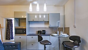Ett kompakt kök med mikrovågsugn, brödrost och vattenkokare, ett litet matbord med två stolar och en soffa.