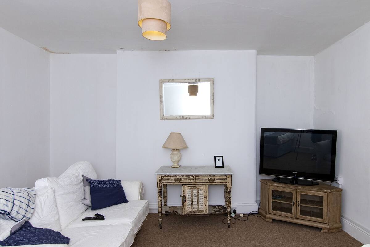 A white room with a white sofa, a small wooden table with a lamp, and a television on a wooden cabinet.