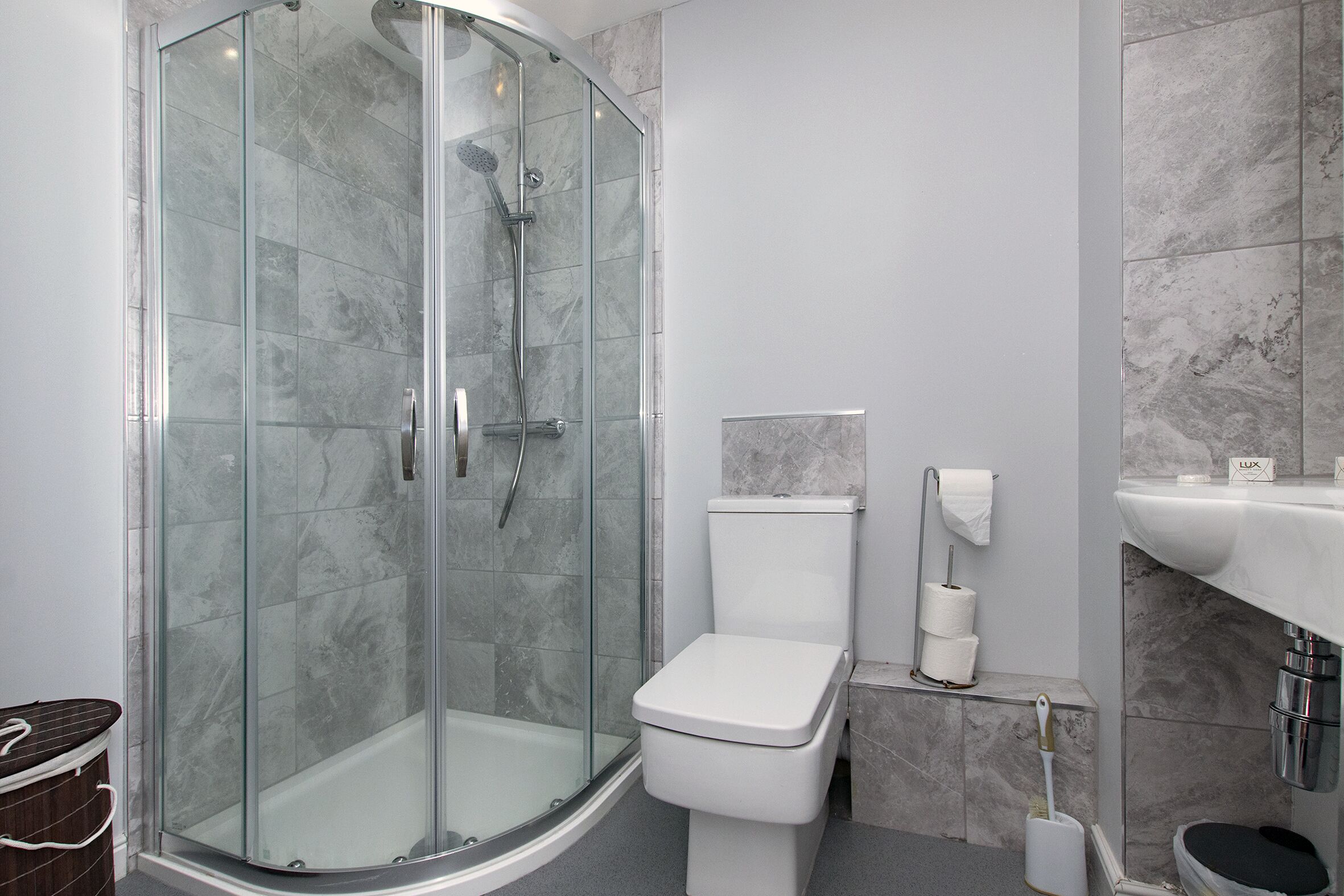 A modern bathroom with a glass-enclosed shower, a white toilet, and a marble-tiled wall.