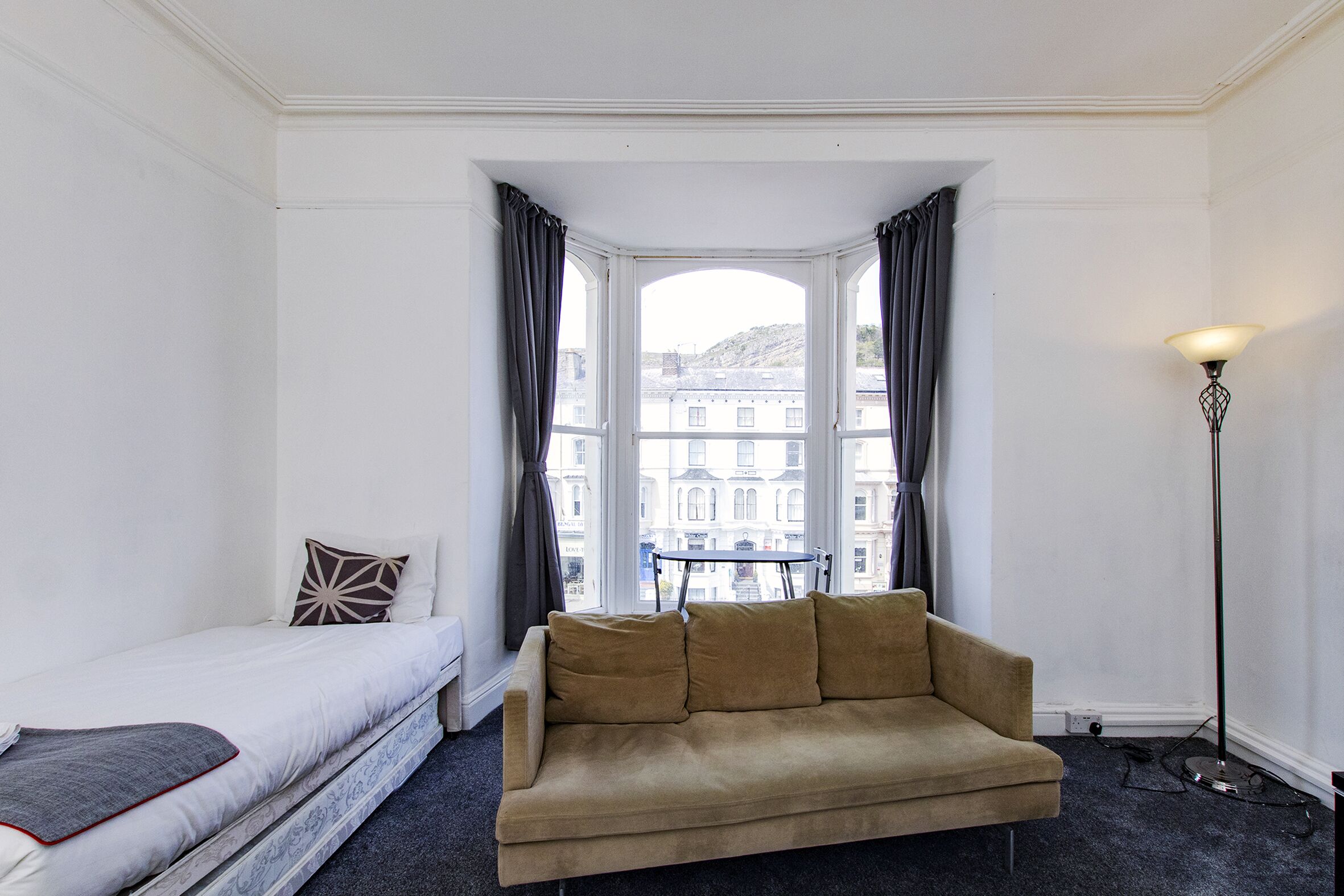 A room with a bed, a sofa, a window with curtains, and a floor lamp.