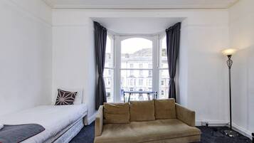 A room with a bed, a sofa, a window with curtains, and a floor lamp.