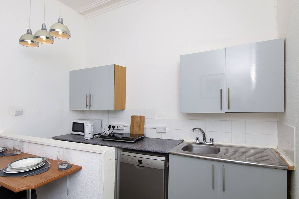 A compact kitchen with grey cabinets, a built-in microwave, a dishwasher, and a sink.