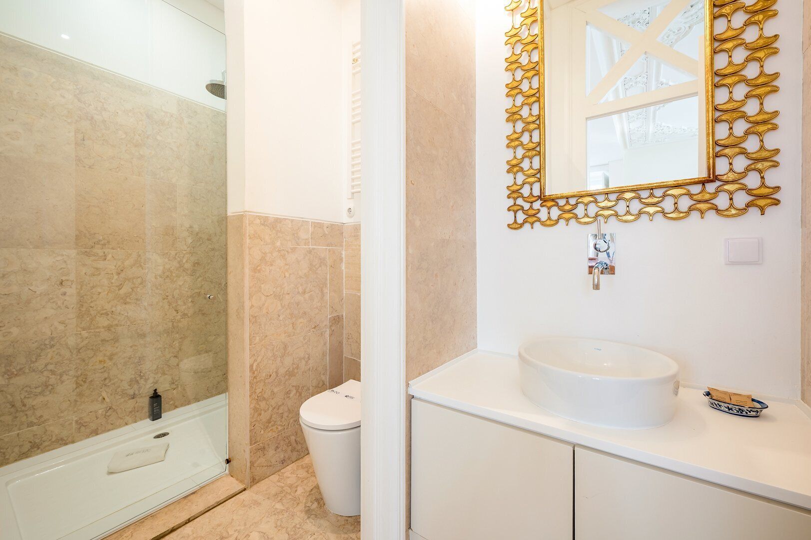 A bathroom with a glass shower enclosure, a white sink, and a gold-framed mirror.