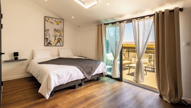 Un dormitorio con cama, mesita de noche, un cuadro y vistas a un espacio exterior a través de un ventanal corredero.