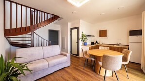 Una sala de estar moderna con una escalera, un comedor con mesa y sillas de madera, y una cocina con armarios y electrodomésticos.