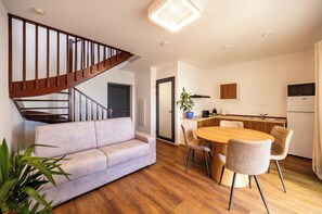 A modern living room with a staircase, a dining area with a wooden table and chairs, and a kitchen with cabinets and appliances. - Duplex Piléa (Saint-Pierre)