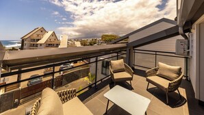 Una terraza en la azotea con mobiliario exterior, barandilla de cristal y vistas al mar y edificios.