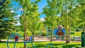 Un parque con juegos infantiles, árboles y un pequeño edificio.