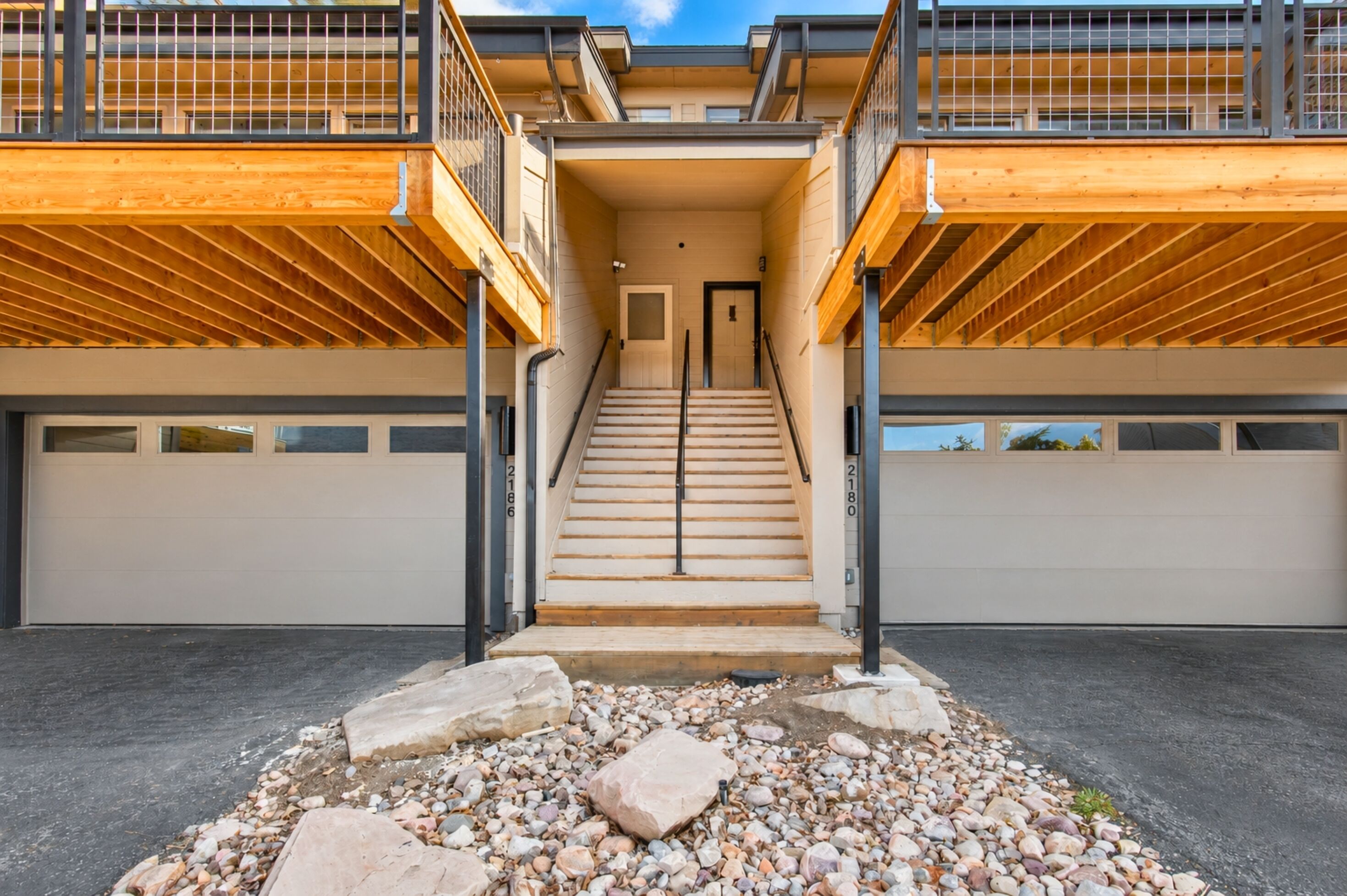 A multi-level residential building with a central staircase, garage doors, and a wooden deck.