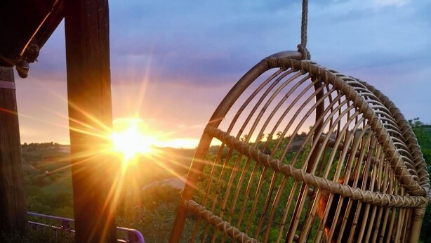 Un fauteuil suspendu en osier sur un balcon, avec vue sur le coucher de soleil.