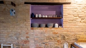 Un mur en pierre sur lequel est fixée une étagère où sont posées des assiettes et des verres.