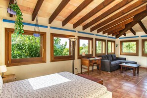 A room with a bed, a sofa, a small table, and multiple windows offering views of greenery. - Verd Salvatge by Rentallorca (Muro)