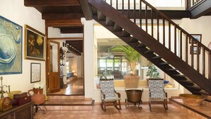 A spacious living area with a wooden staircase, a dining table with chairs, and a view through a large window. - Verd Salvatge by Rentallorca (Muro)
