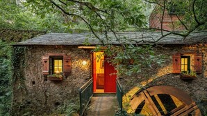 A rustic stone house with a wooden staircase leading to a red door, a large wooden wheel, and a stone wall. - Be&See In River (Ovar)