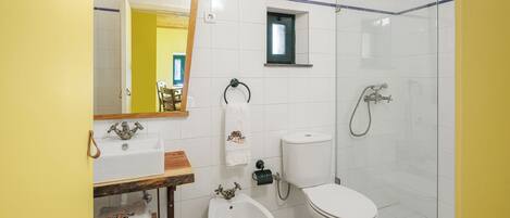 Un baño con lavamanos blanco, bidé, inodoro y cabina de ducha de vidrio.