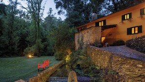 A stone bridge over a stream, a red bench, and a building with windows and a stone facade. - Be&See In River (Ovar)