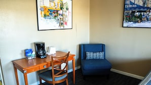 Ein Hotelzimmer mit Holzschreibtisch, einem Sessel, einer blauen Couch und zwei gerahmten Kunstwerken an den Wänden.