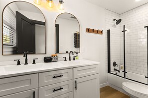 Un baño moderno con un lavabo blanco, dos espejos, una ducha y un inodoro.