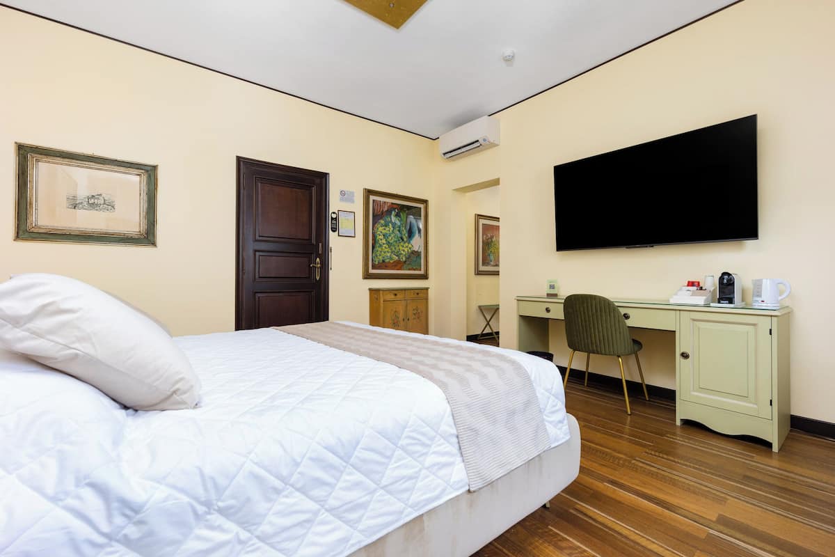 A hotel room with a bed, a desk, a chair, and a flat-screen TV.
