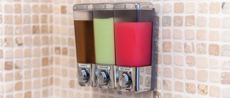 A wall-mounted dispenser with three compartments labeled for shampoo, conditioner, and body wash.