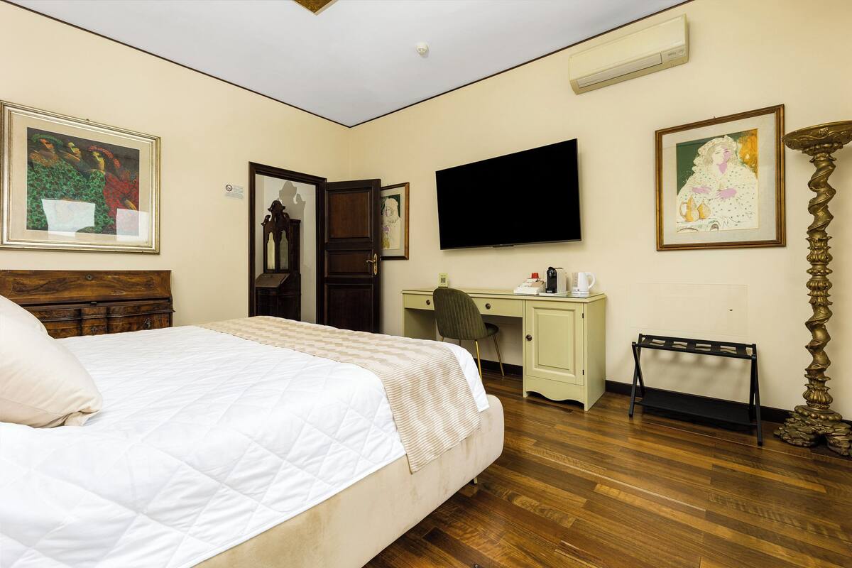 A hotel room with a bed, a desk, a chair, a TV, and artwork on the walls.