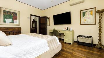 A hotel room with a bed, a desk, a chair, a TV, and artwork on the walls.