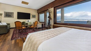 A hotel room with a large bed, a desk with a chair, a television, and a view of the city through large windows. - Reggio Suite Luxury B&B (Reggio Calabria)