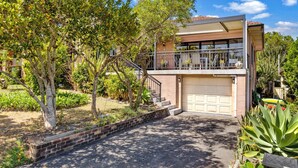 A two-story house with a garage, surrounded by a garden with various plants and trees. - View Street Lake House (The Entrance)