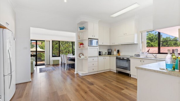 A modern kitchen with white cabinets, a built-in oven, and a dining area with a table and chairs. - View Street Lake House (The Entrance)
