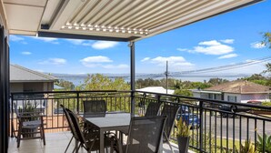 A covered balcony with a table and chairs, overlooking a residential area and a body of water. - View Street Lake House (The Entrance)