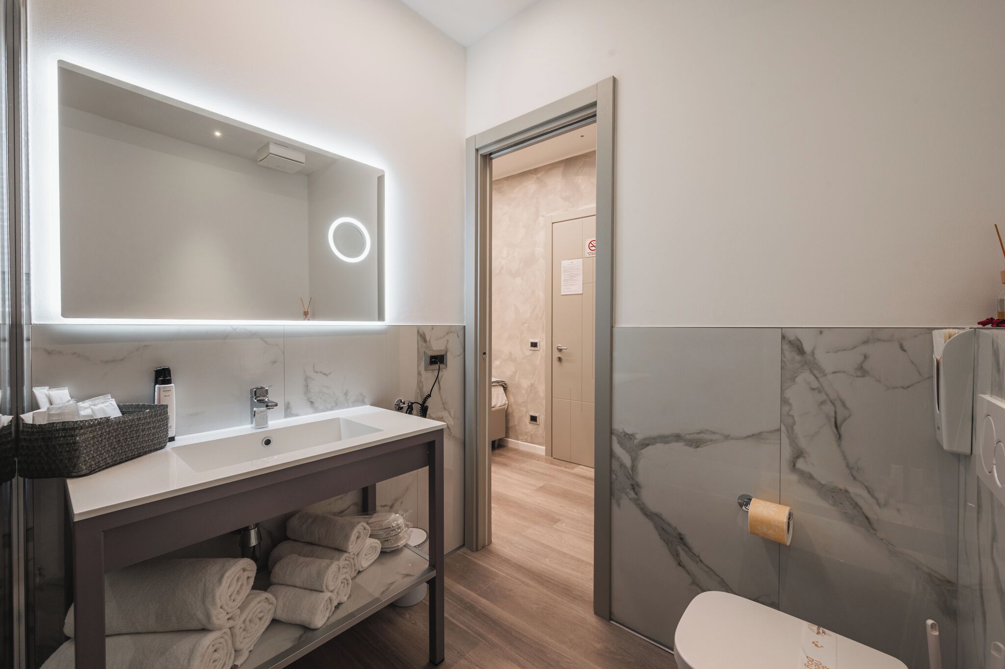 A modern bathroom with a large mirror, a sink, a vanity with towels, and a shower area.
