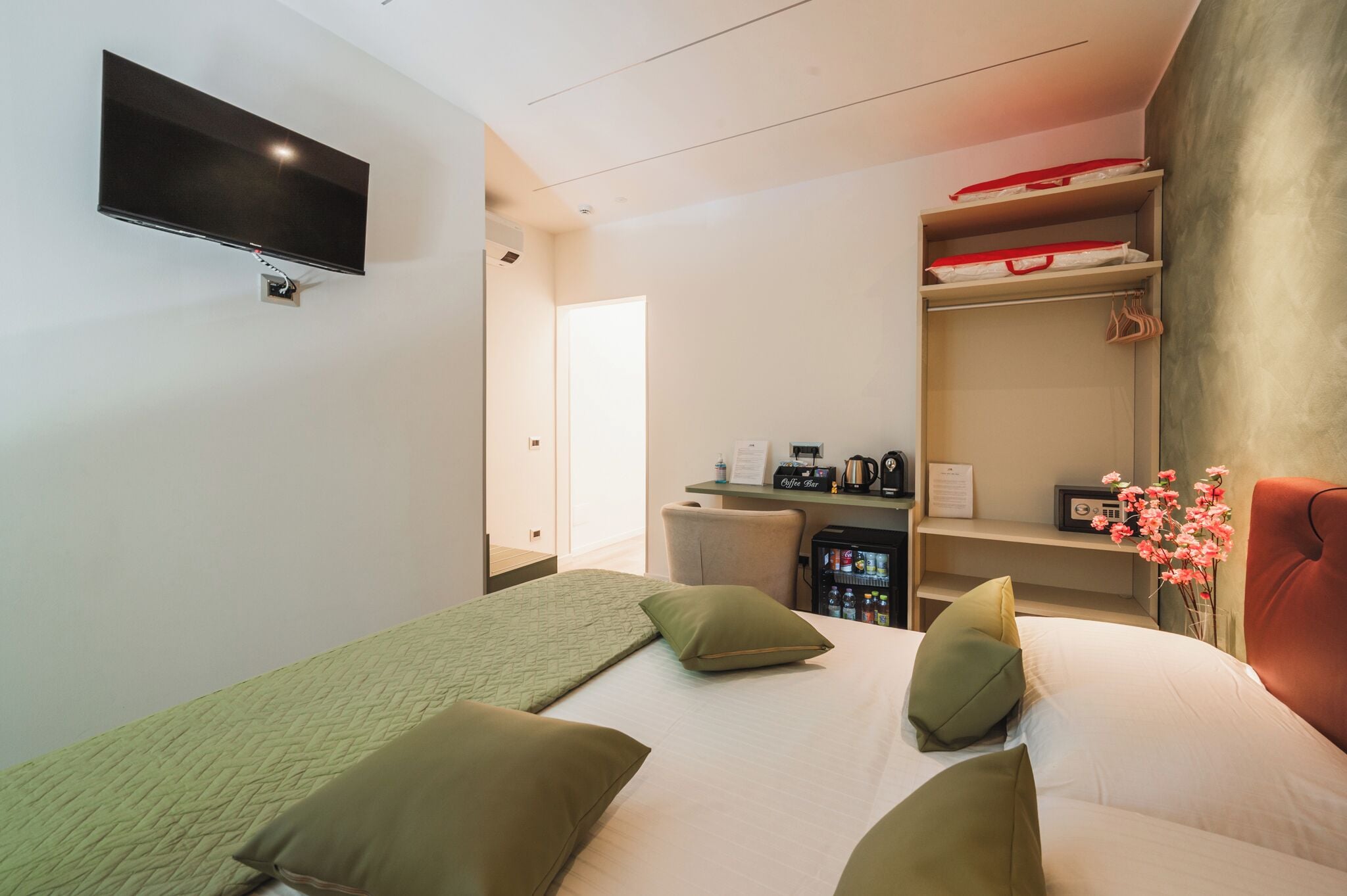 Ein Hotelzimmer mit einem Bett, einem an der Wand befestigten Fernseher, einer Kaffeemaschine und einer kleinen Küchenzeile.